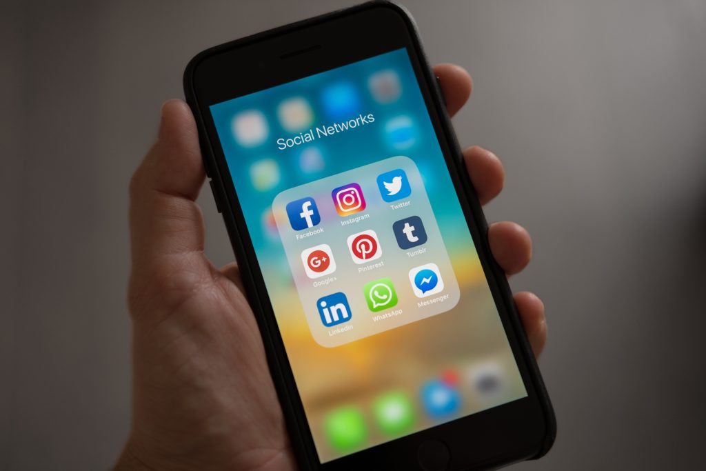 iphone being held by a hand displaying social media apps like facebook, instagram, twitter, linkedIn